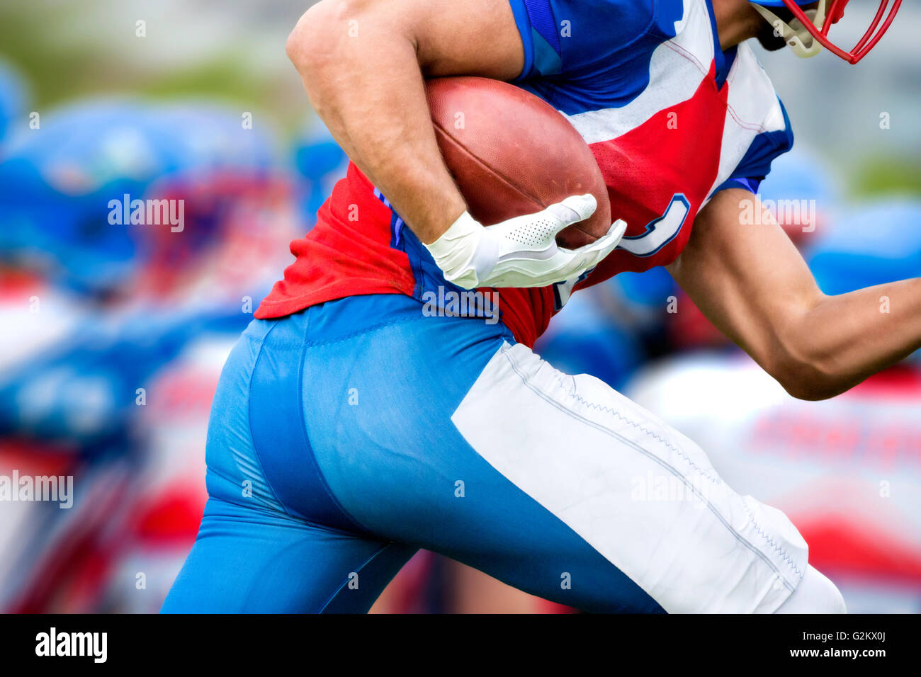 Vista laterale del giocatore di football americano che corre con la palla per rendere un touchdown. Foto Stock