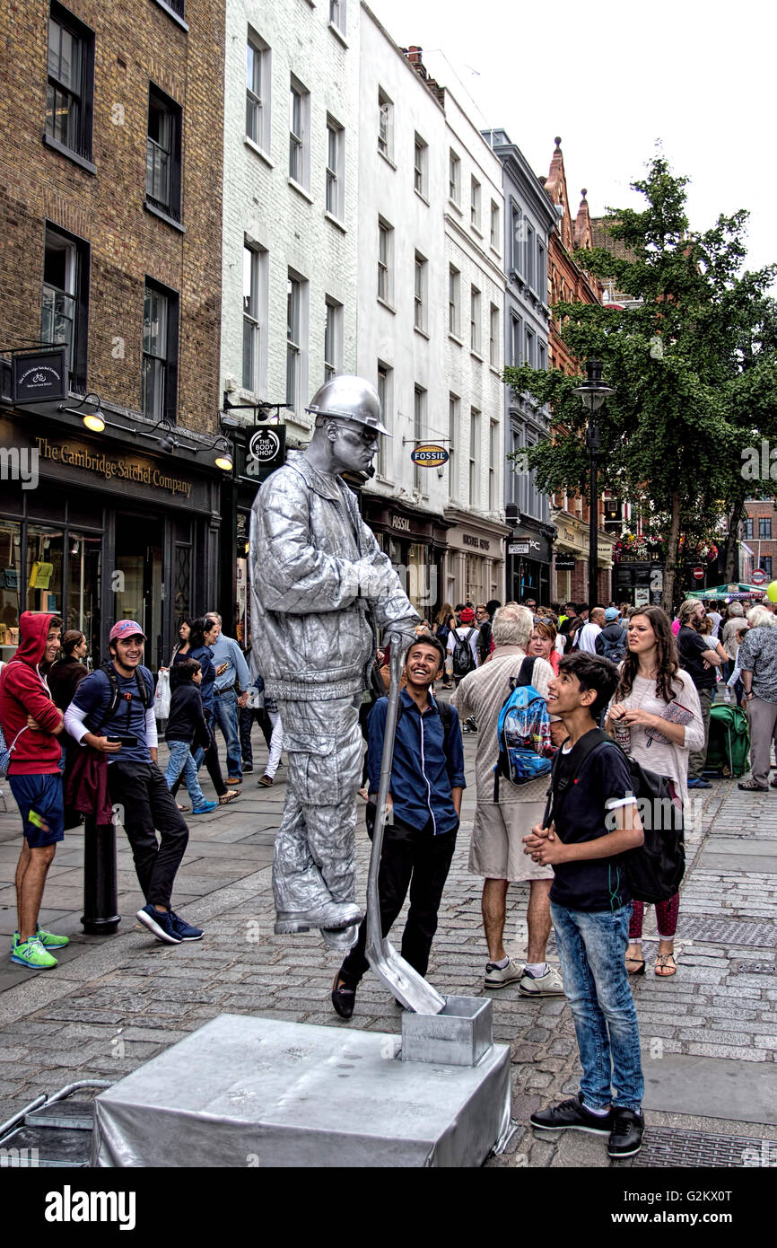I turisti guardano ad un levitating artista di strada vestito come Un costruttore d'argento a Covent Garden London Foto Stock