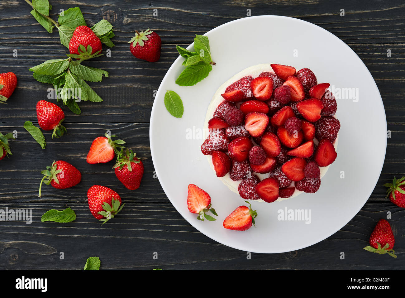 Berry pan di spagna con fragole, lamponi e crema decorate con foglie di menta sul legno scuro dello sfondo. Top vie Foto Stock