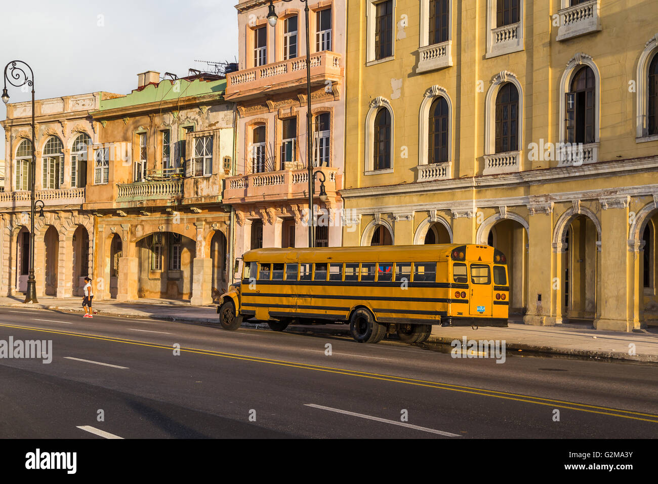 Una vecchia scuola di giallo autobus parcheggiato sul lato di Malecon ocean autostrada a l'Avana. Foto Stock