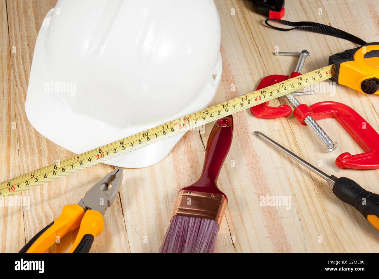 Disco bianco hat posa su un pavimento di legno con una varietà di operaio di utensili a mano Foto Stock