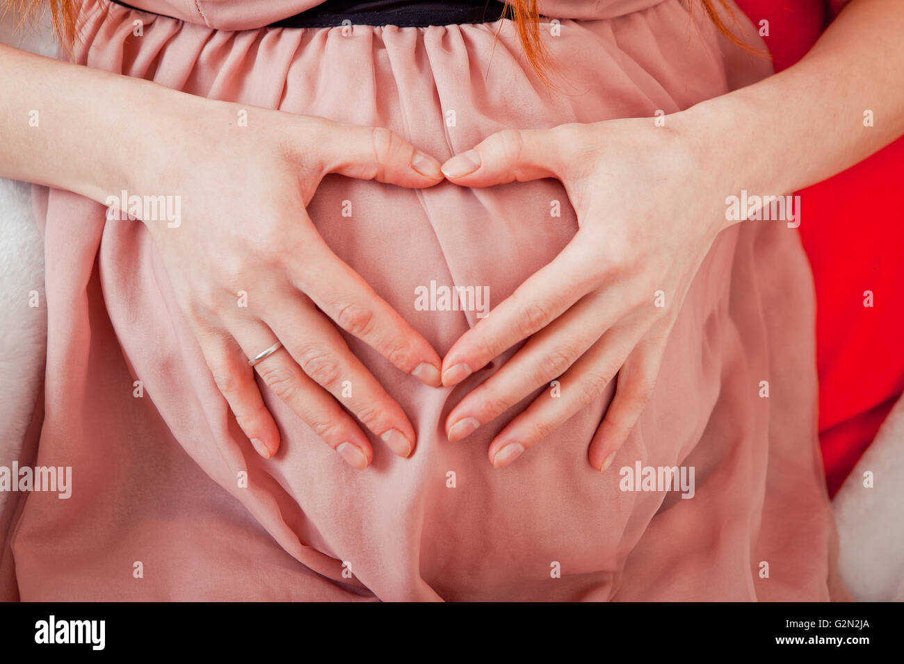 Donna incinta tenendo le sue mani a forma di cuore sul suo bambino bump. Pancia in gravidanza con le dita il simbolo del cuore. Concetto di maternità. Baby Shower Foto Stock