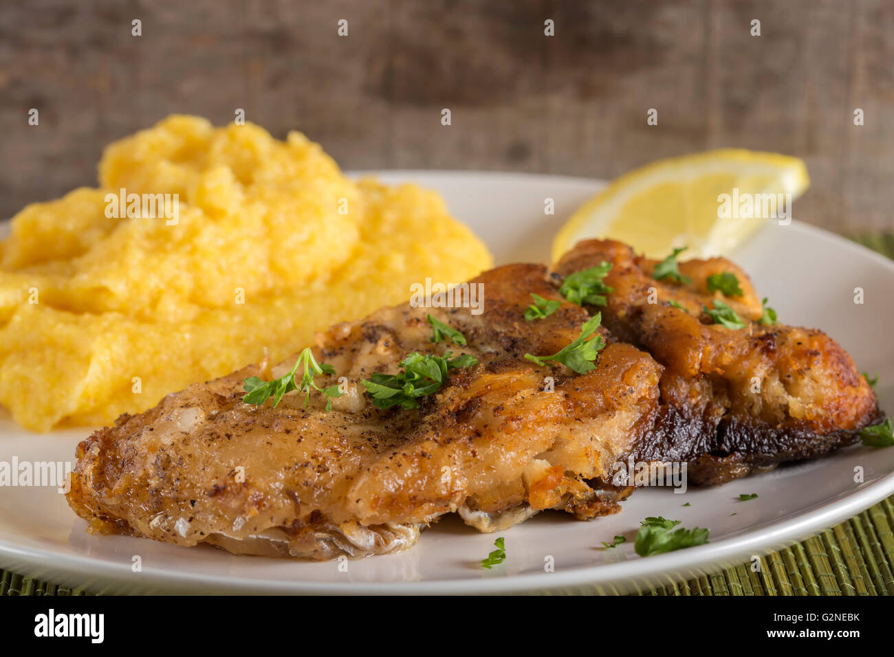 Pesce fritto con polenta e succo di limone sulla piastra Foto Stock