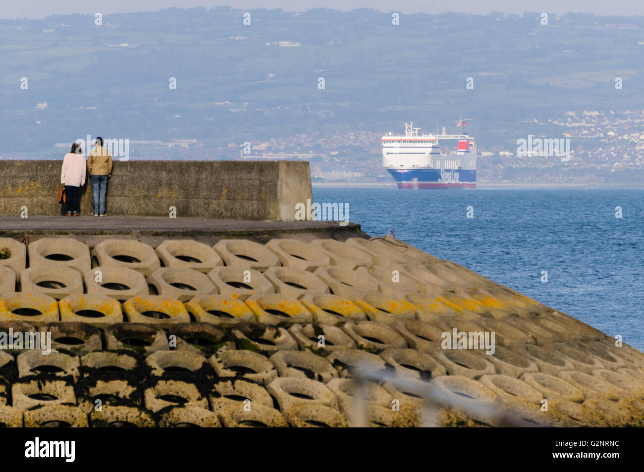 Bangor, County Down. 23/09/2012 - Due membri del pubblico stand alla fine di un molo, guardando un grande Stena Line traghetto barca a vela lungo il Belfast Lough. La nave è seduto ad alto contenuto di acqua come il trasporto di peso molto ridotto. Foto Stock