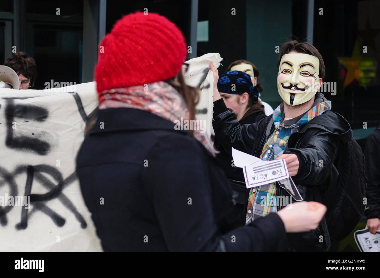 Un giovane uomo che indossa una maschera di Guy Fawkes, sinonimo con il gruppo di hacker 'Anonimo' mani un foglietto illustrativo di un passerby durante una manifestazione di protesta contro la legislazione di internet. Belfast 11/02/2012 Foto Stock
