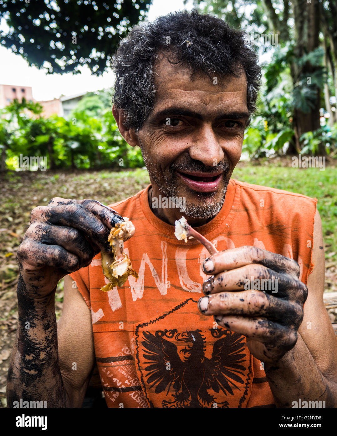 Un meccanico con le mani unte prende una pausa pranzo nel Parco Laureles Medellin in Colombia Foto Stock