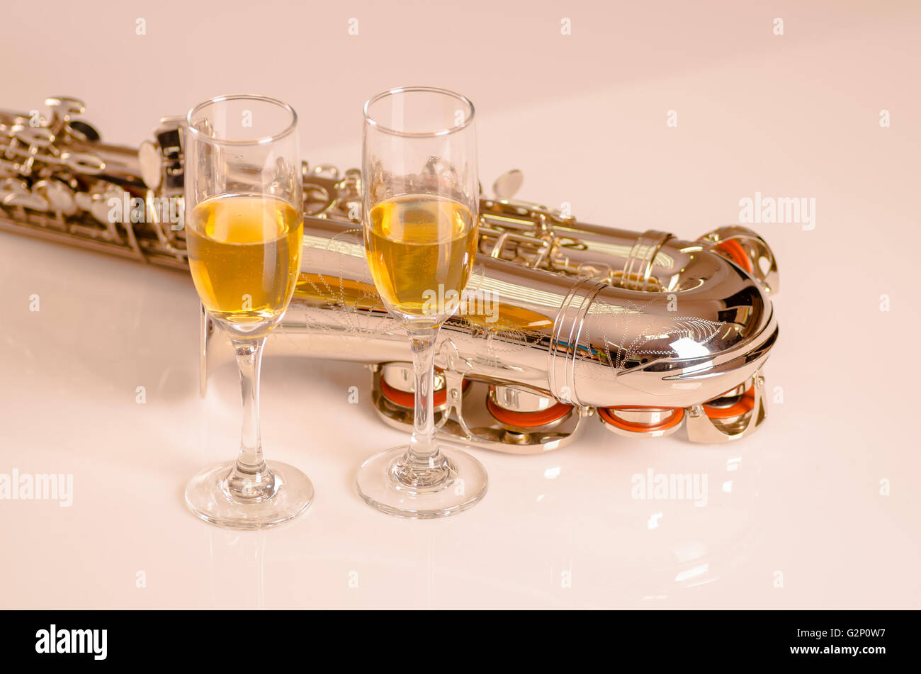 Shiny sassofono giacente sulla superficie bianca, note musicali di carta e due bicchieri di champagne seduto accanto ad esso Foto Stock