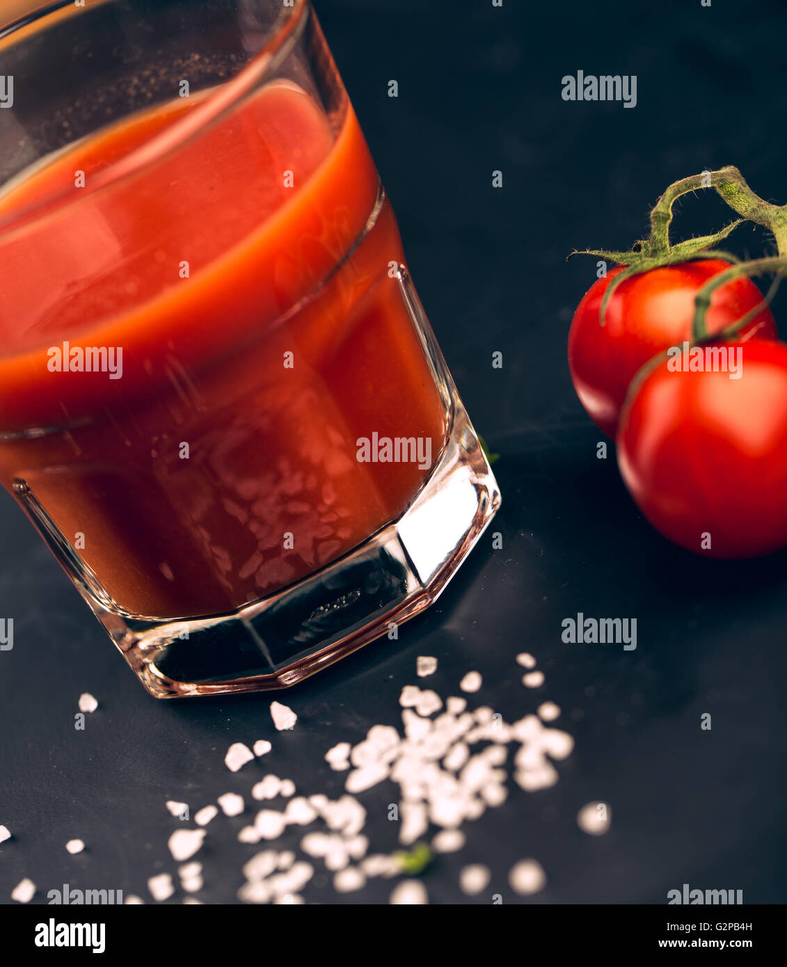 I succhi di pomodoro e i pomodori freschi sul nero ardesia con sale grosso Foto Stock