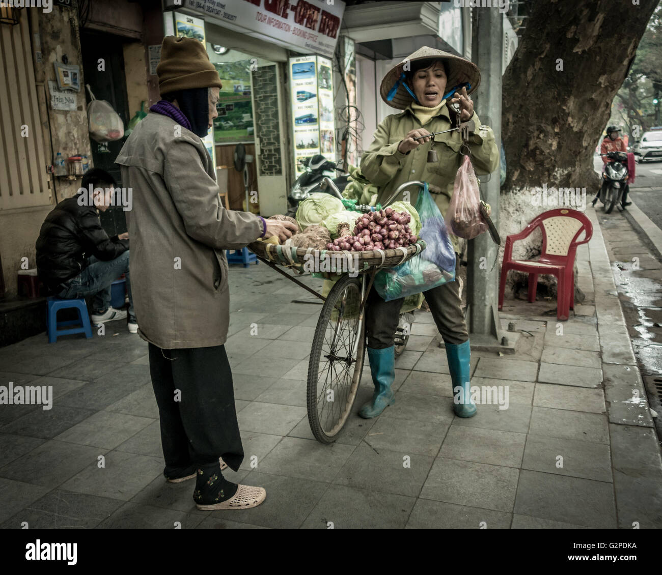 La donna in sella a una moto la vendita di verdure fresche, con i tradizionali strumenti di pesatura indossando abiti tradizionali della cultura locale, Hanoi, Vietnam Foto Stock