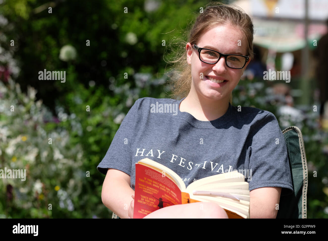 Festival di fieno, Wales, Regno Unito - Giugno 2016 - Una giovane donna che indossa un Festival di fieno tee shirt la lettura di un libro in brossura sui prati del Festival. Foto Stock