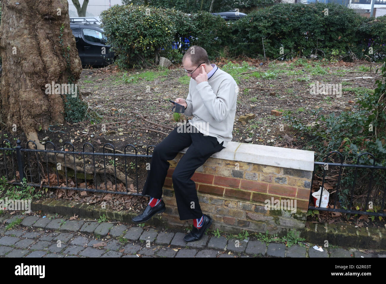 Uomo che indossa unione jack calze siede sulla parete parlando al telefono nella zona di Hampstead a Londra Foto Stock