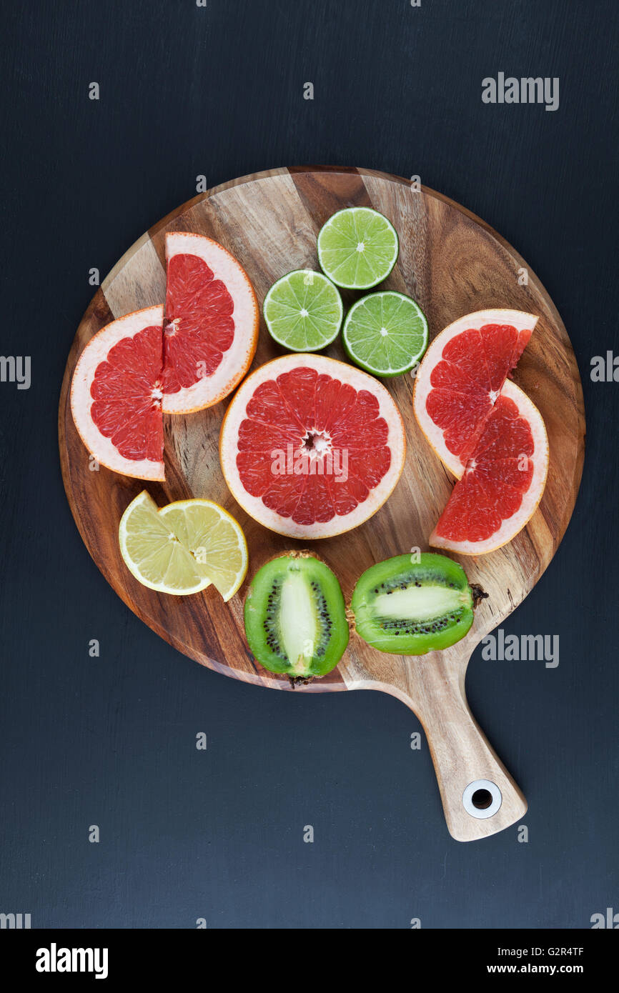 Fette di pompelmo rosso, limone, kiwi, e calce di acacia tagliere. L'immagine verticale con spazio di copia Foto Stock