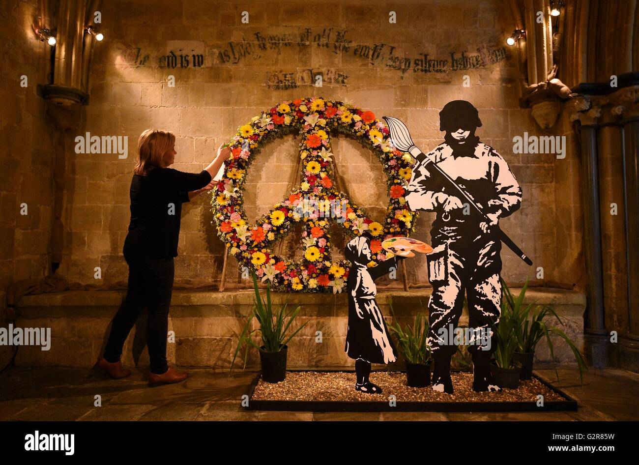 Un fiorista rende i tocchi finali a un Bansky ispirato pezzo intitolato "Date una possibilità alla pace' che accoglie i visitatori a Chichester Cathedral annuale del Festival dei Fiori, che quest anno ha per tema "l'artisti Tavolozza'. Foto Stock