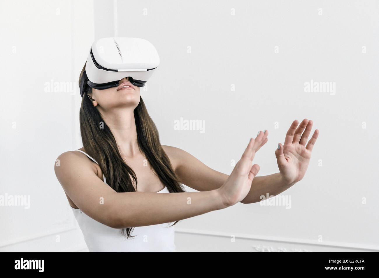 Una giovane donna bianca con i capelli scuri sta con le braccia tese a sentire e di senso con una realtà virtuale heasdet sul suo capo Foto Stock