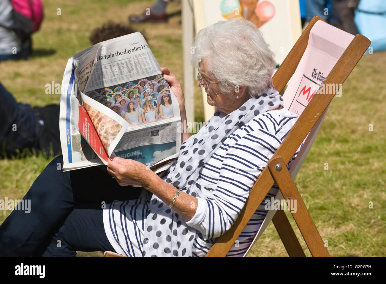 Signora anziana giornale di lettura sat in sedia a sdraio sul prato a Hay Festival 2016 Foto Stock