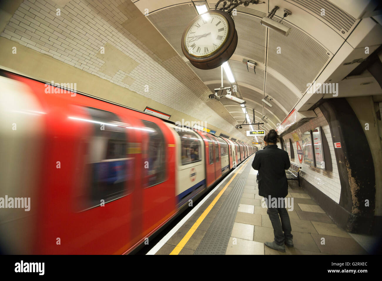 Un giovane uomo vestito di nero in piedi accanto a un movimento di treno sotterraneo alla linea centrale a Londra, Inghilterra. Foto Stock