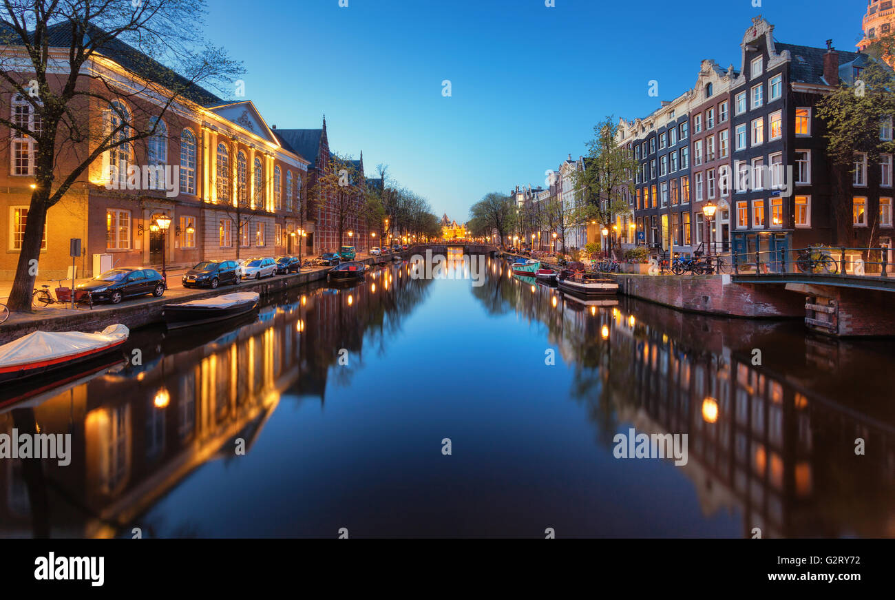 Bellissimo paesaggio urbano di notte a Amsterdam, Paesi Bassi. Riflette le luci della città in acqua con il blu del cielo. Illuminazione notturna della sede, Foto Stock