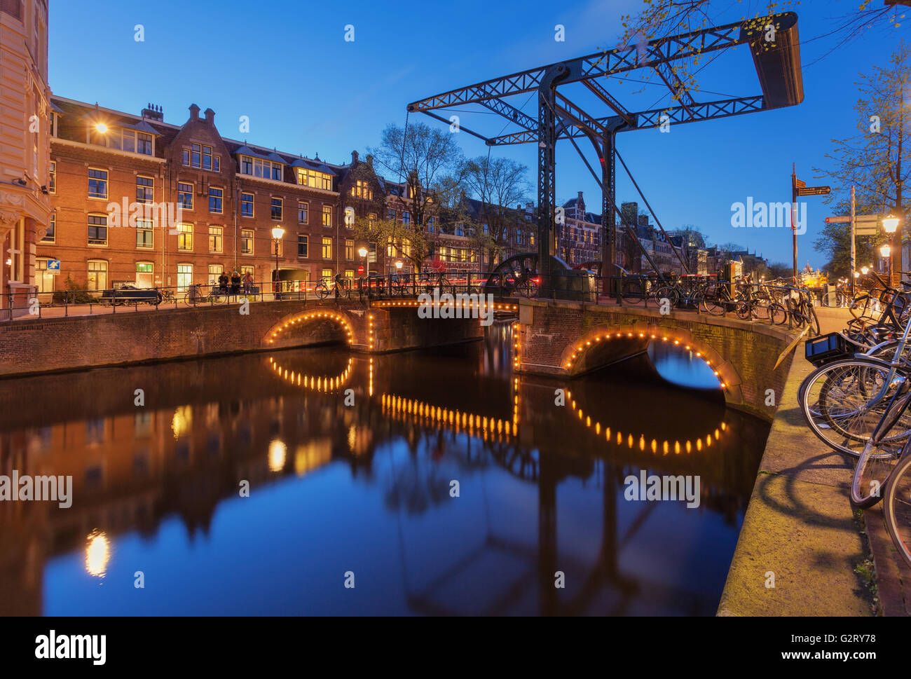 Bellissimo paesaggio urbano di notte a Amsterdam, Paesi Bassi. Riflette le luci della città in acqua con arco e cielo blu. Illuminazione notturna o Foto Stock