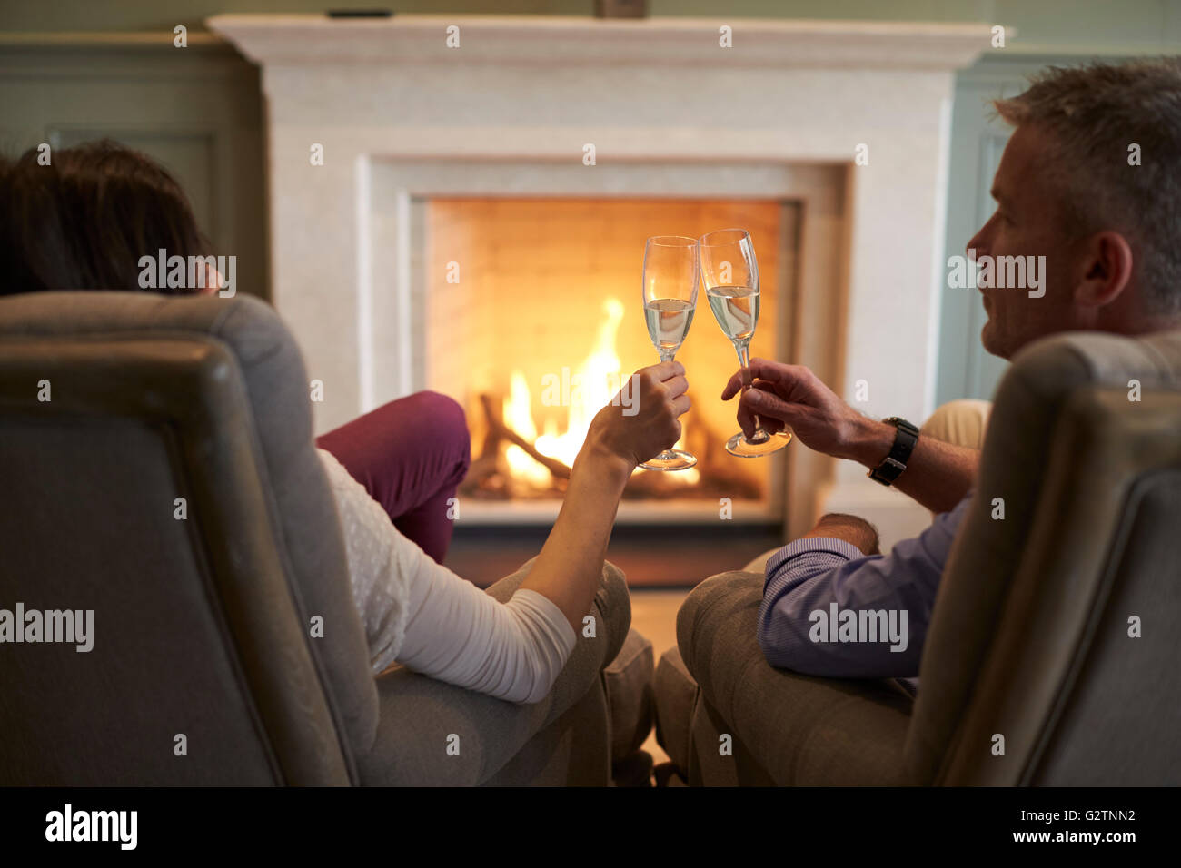 Coppia seduta dal fuoco facendo Toast con Champagne Foto Stock