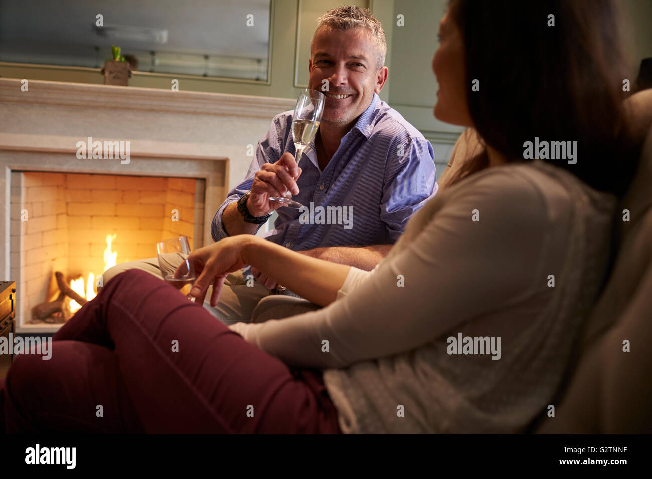 Coppia Matura seduti davanti al caminetto di bere champagne Foto Stock