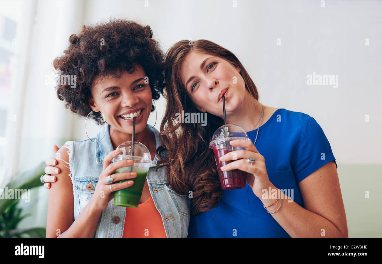 Ritratto di giovane e bella donna di bere succo di frutta fresco insieme. Amici di sesso femminile in piedi insieme con succo di frutta. Foto Stock