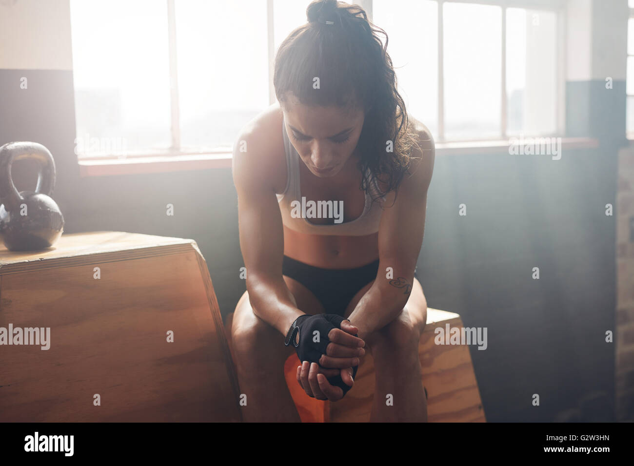 Giovane donna seduta su una casella in palestra dopo il suo allenamento e guardando verso il basso. Atleta femminile prendendo riposo dopo un allenamento in palestra Foto Stock