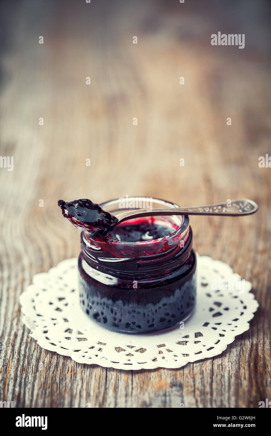 Un vasetto di marmellata con cucchiaio sul vecchio tavolo in legno. Retrò tonica. Foto Stock