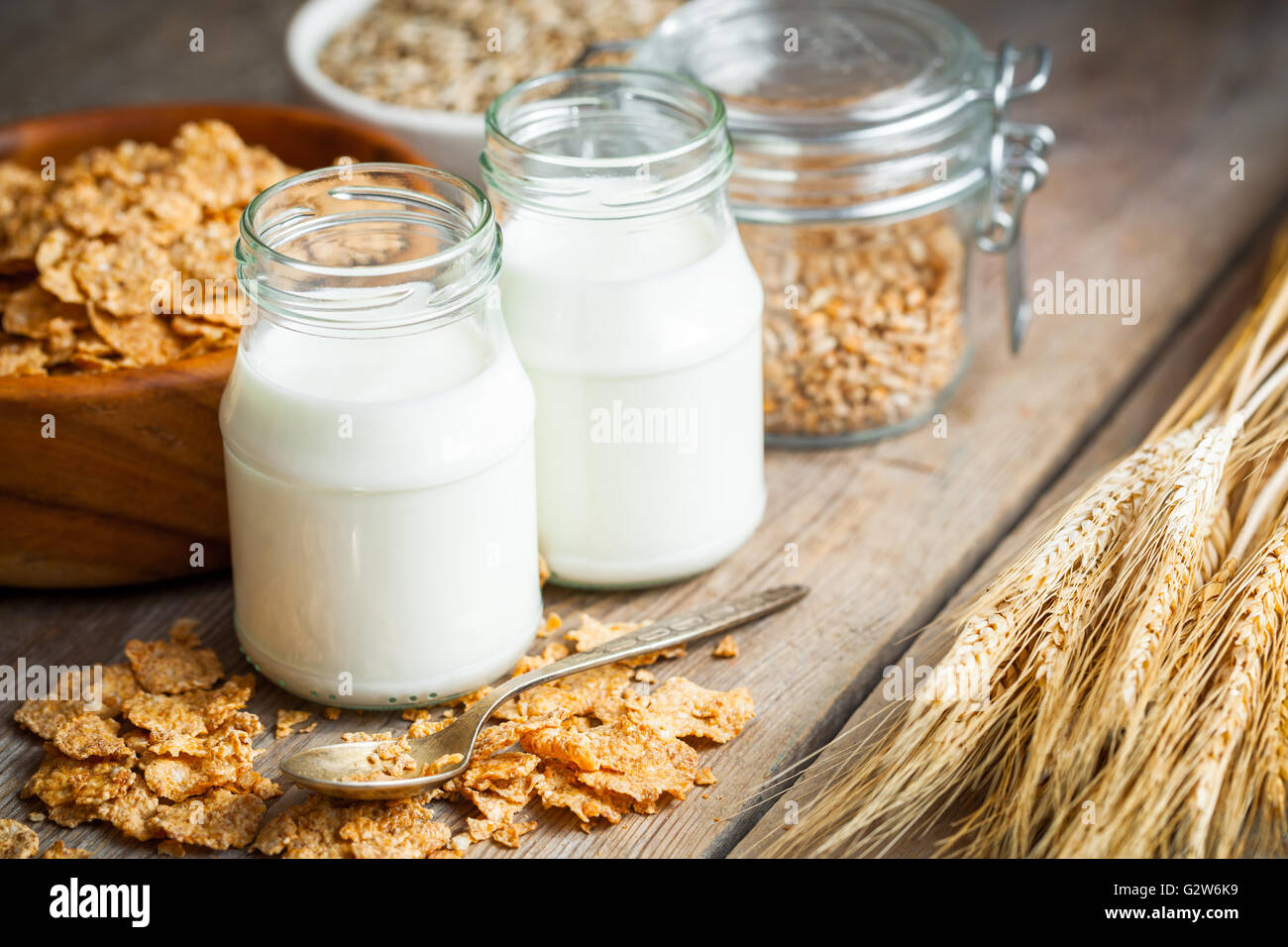 Colazione a base di cereali fiocchi di frumento, picchi e bottiglie di latte sul tavolo di legno Foto Stock