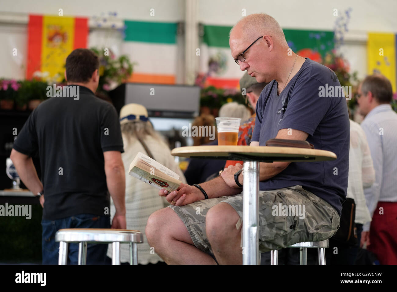 Festival di fieno, Wales, Regno Unito - Giugno 2016 - L'uomo gode il meglio di entrambi i mondi con un libro e una birra in uno dei bar del fieno sito del Festival. Foto Stock