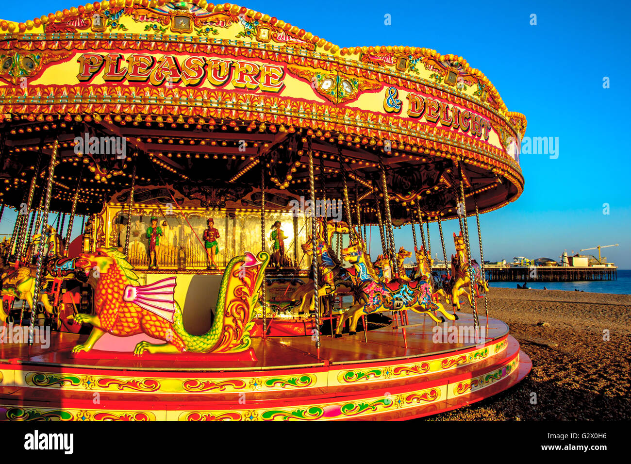 Una giostra sulla spiaggia di Brighton con pier su sfondo, East Sussex, Inghilterra Foto Stock