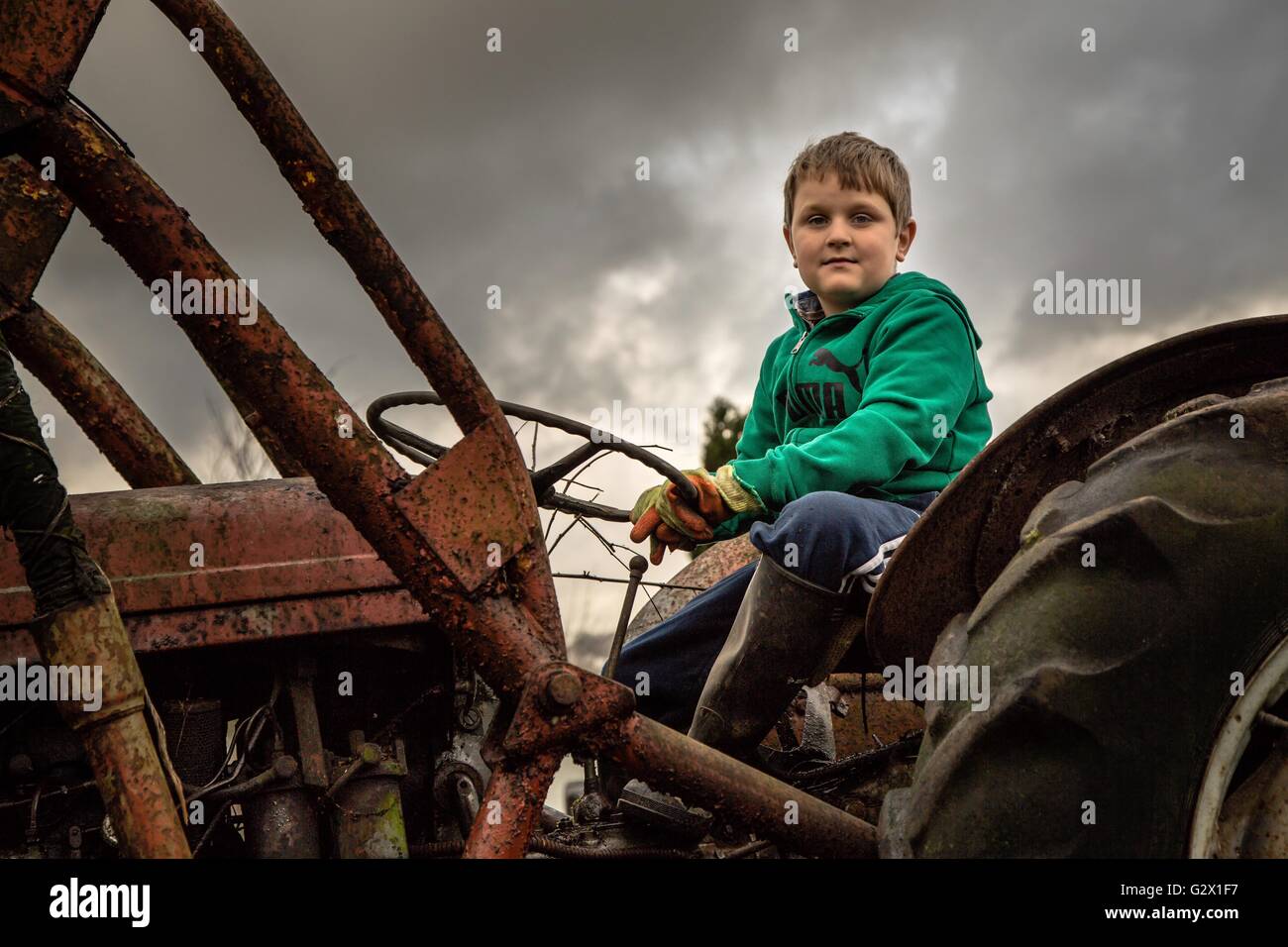 Giovane ragazzo sui suoi nonni trattore durante un giorno nuvoloso Foto Stock