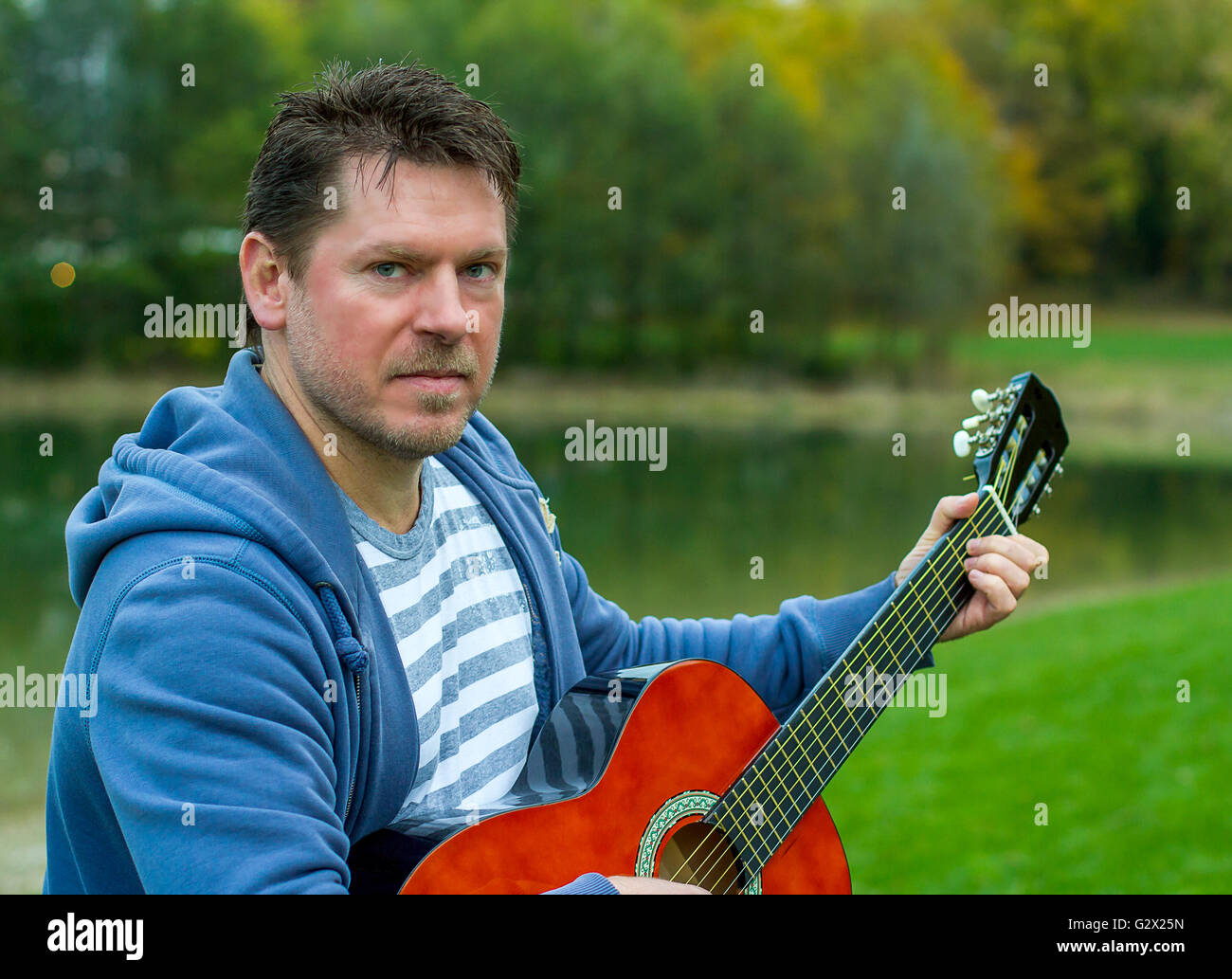 Maturo uomo barbuto suonare chitarra rossa nel parco verde in riva al lago Foto Stock