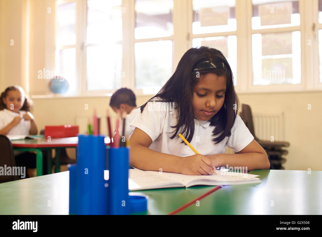 Pupilla d femmina a lavorare alla scrivania nella scuola elementare Classroom Foto Stock