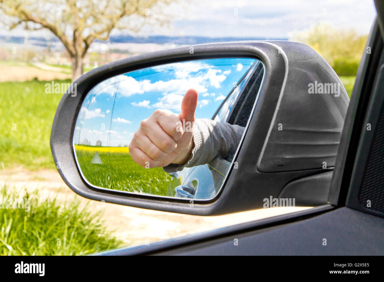 Uomo con il pollice fino a specchio laterale di una automobile Foto Stock