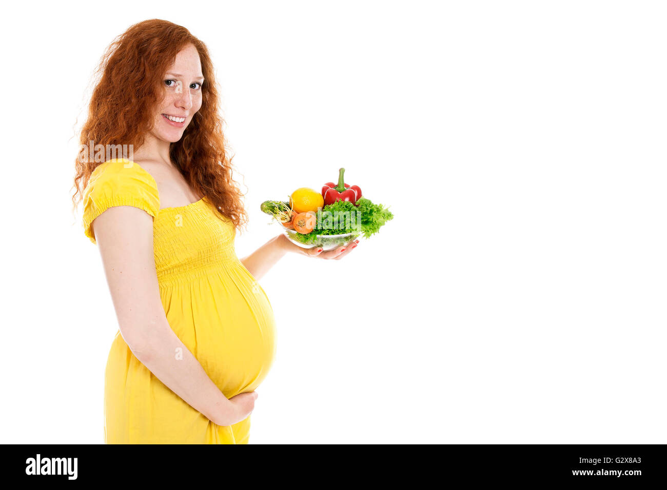 Donna incinta tenendo le verdure e sorridente Foto Stock