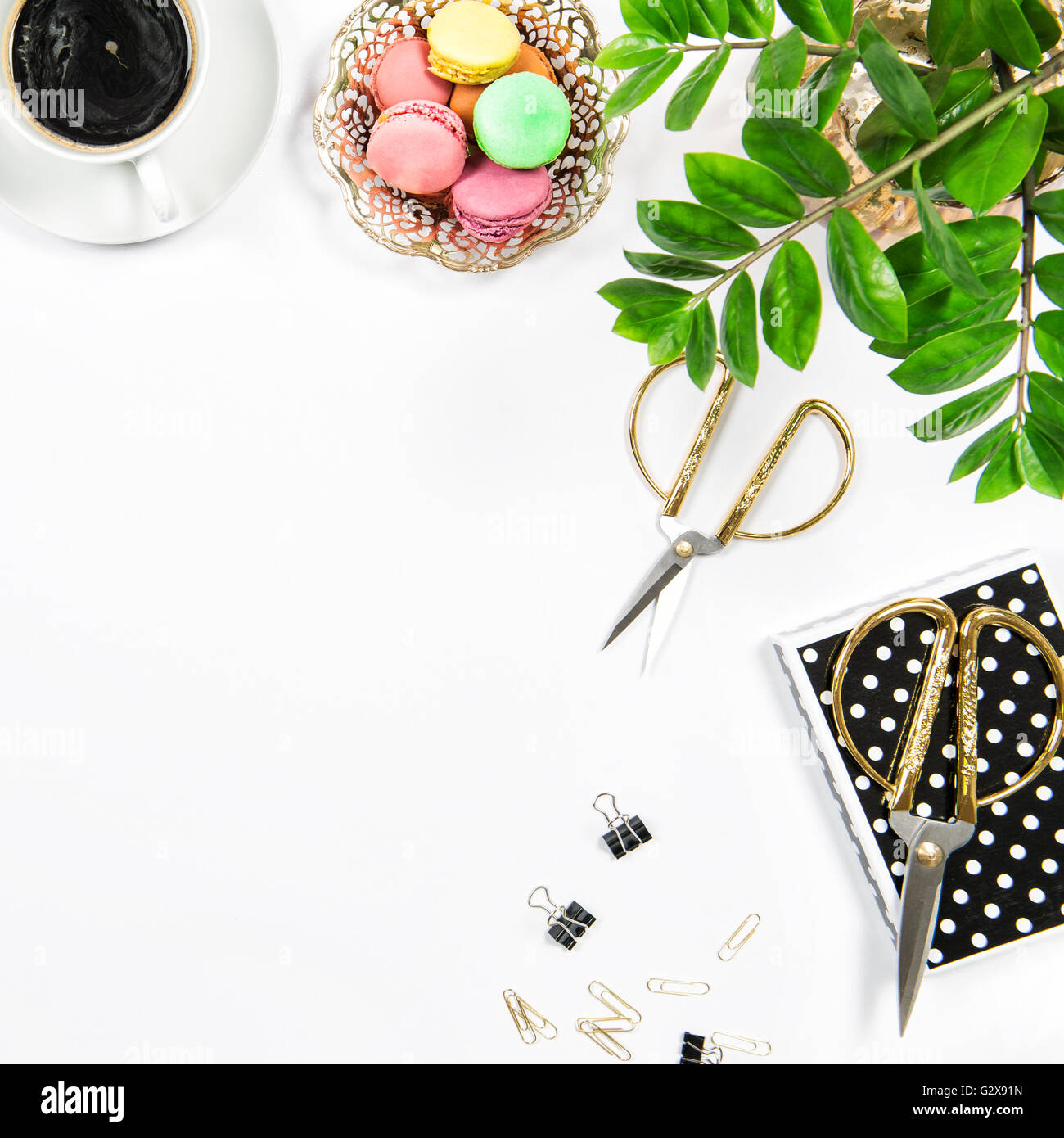 Posto di lavoro femminile con caffè, macarons cookie, forniture da ufficio e di pianta verde su bianco sfondo tabella. Lay piatto Foto Stock
