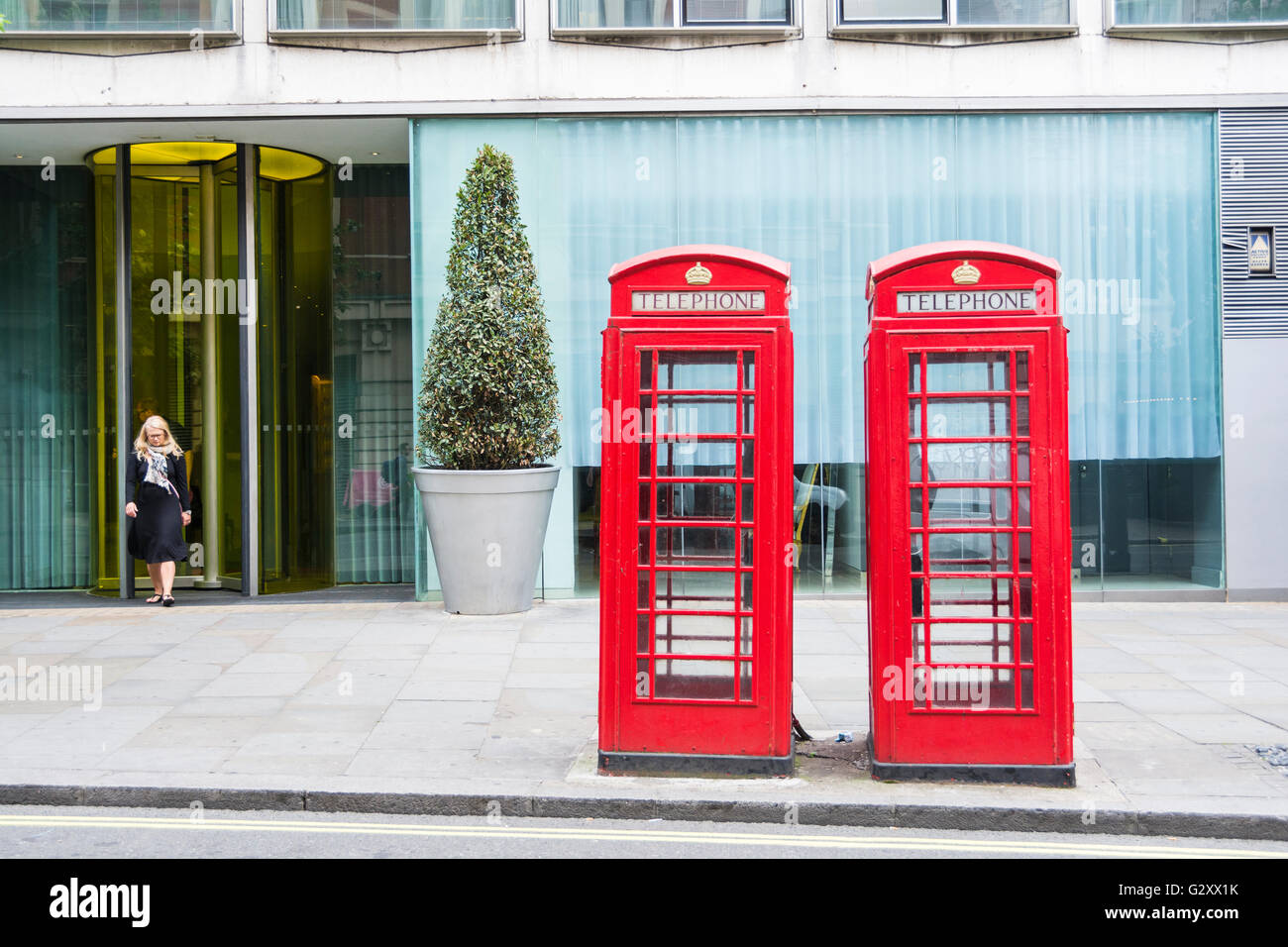 Una donna emerge da una porta d'ufficio dietro due chioschi telefonici di grado II elencati Sir Giles Gilbert Scott K6 London, Londra, Inghilterra, Regno Unito Foto Stock