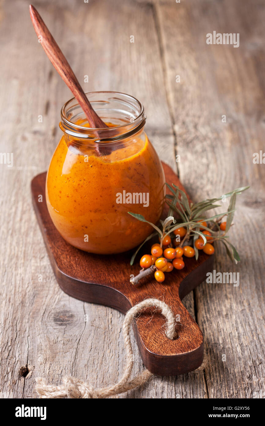 Vaso di vetro con bacche di olivello spinoso jam su uno sfondo di legno Foto Stock
