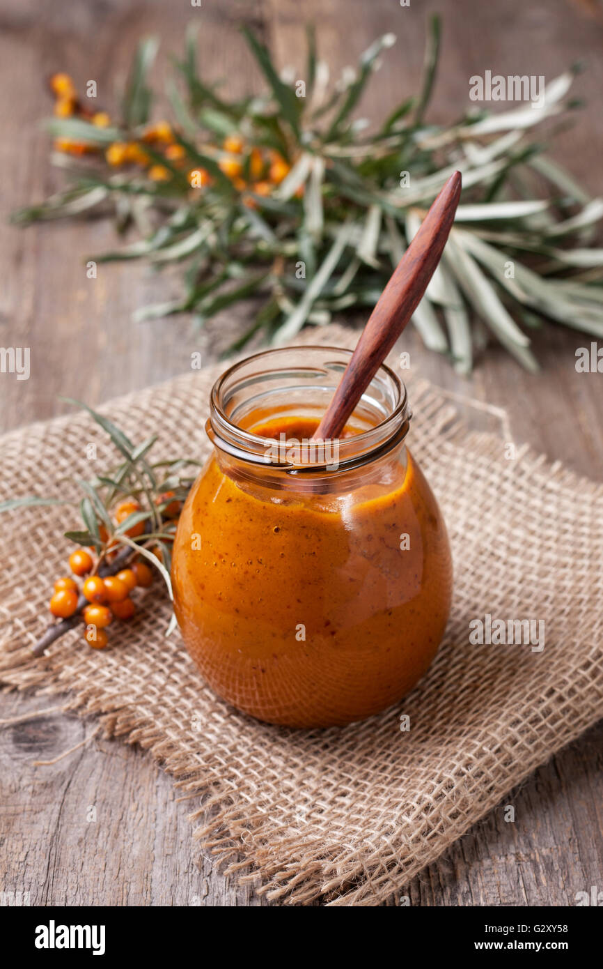 Vaso di vetro con bacche di olivello spinoso jam su uno sfondo di legno Foto Stock