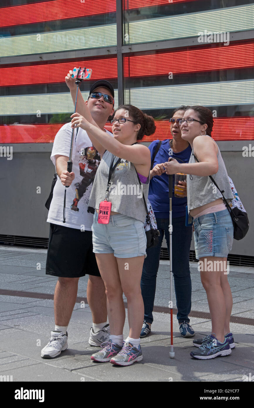 Una famiglia di turisti asiatici posano per una selfie nella parte anteriore del quadro elettrico di bandiera americana in Times Square e Midtown Manhattan, New York Foto Stock