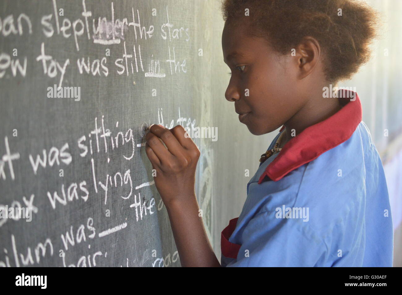 Ragazza giovane completando un gap esercizio di riempimento su una lavagna a Malasang scuola primaria, Buka, Bougainville, Papua Nuova Guinea Foto Stock