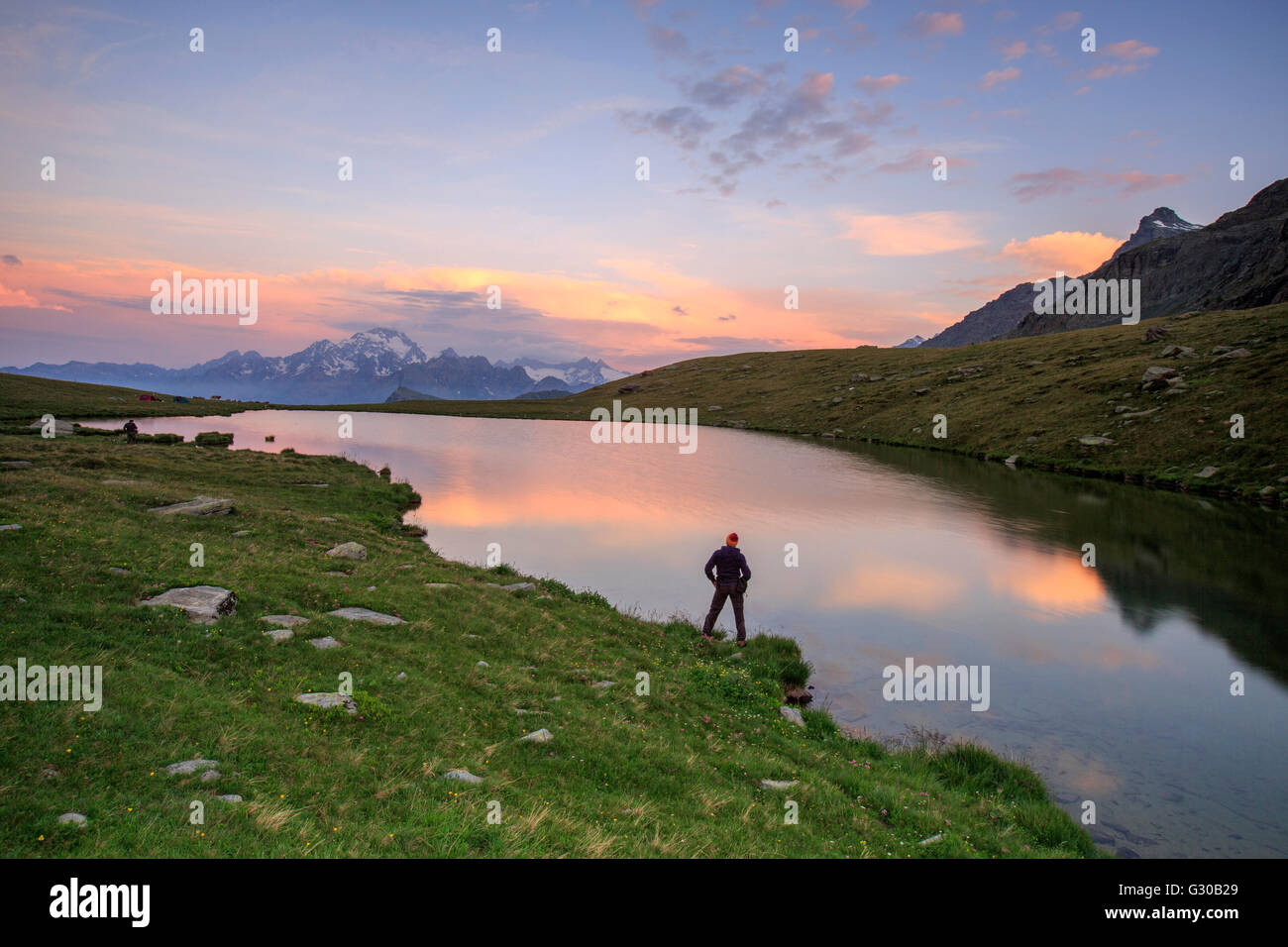 Escursionista sulla riva ammira i colori rosa di alba riflessa nel lago Campagneda, Malenco Valley, Valtellina, Lombardia, Italia Foto Stock