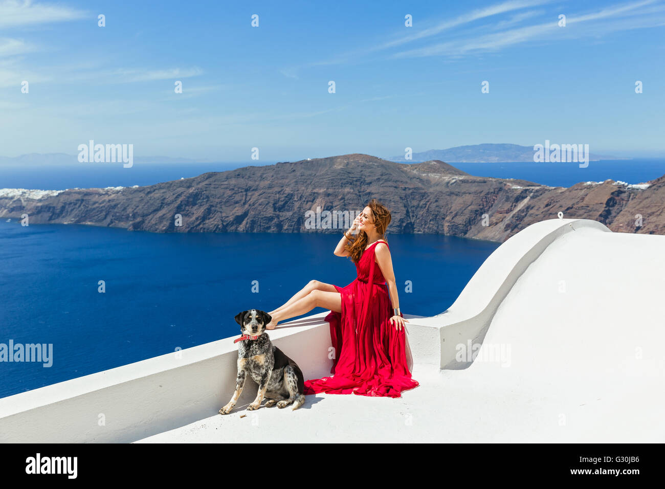 Donna in abito rosso sul bordo del tetto, guardando il mare nei pressi di un bellissimo cane Foto Stock