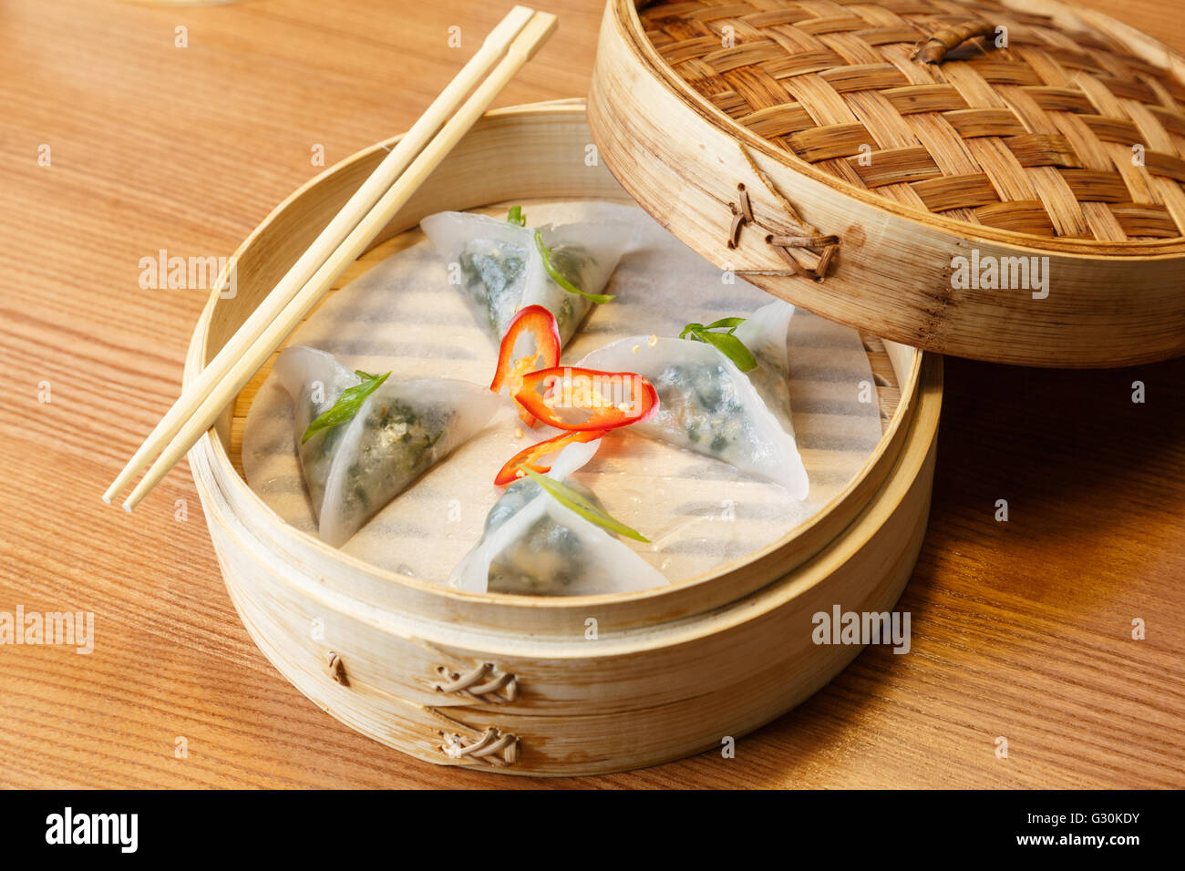 Dim somme con spinaci e tofu formaggio in un sistema per la cottura a vapore in bambù sul tavolo di legno nel ristorante asiatico Foto Stock