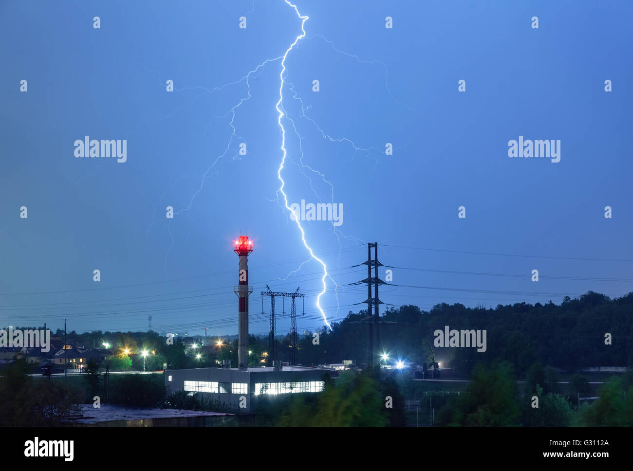 Un fulmine nel cielo notturno sopra il locale caldaie e linee di alimentazione Foto Stock