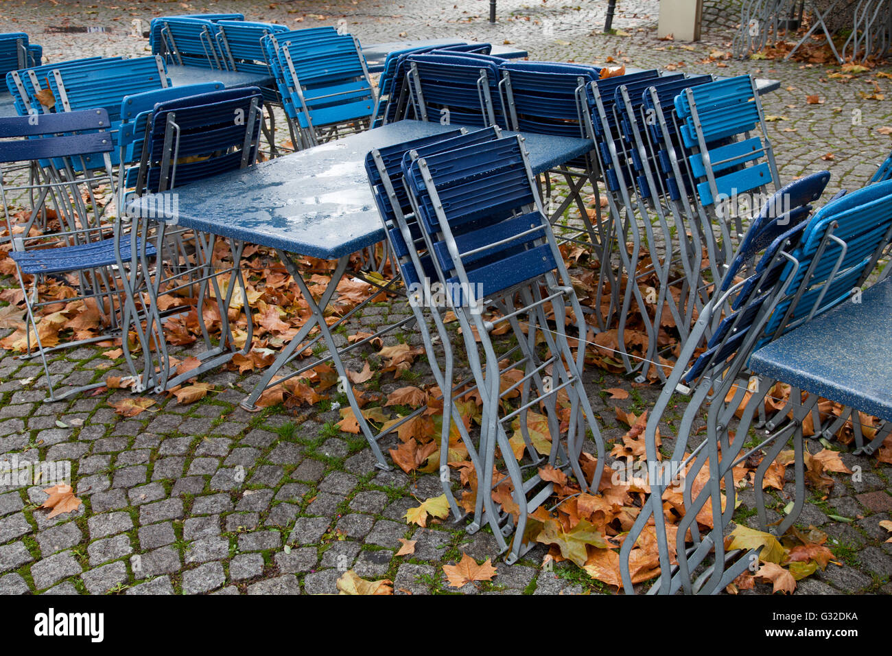Svuotare i tavoli e le sedie di una sala da pranzo all'aperto sotto la pioggia con foglie di autunno nel centro storico di Colonia, nella Renania Foto Stock
