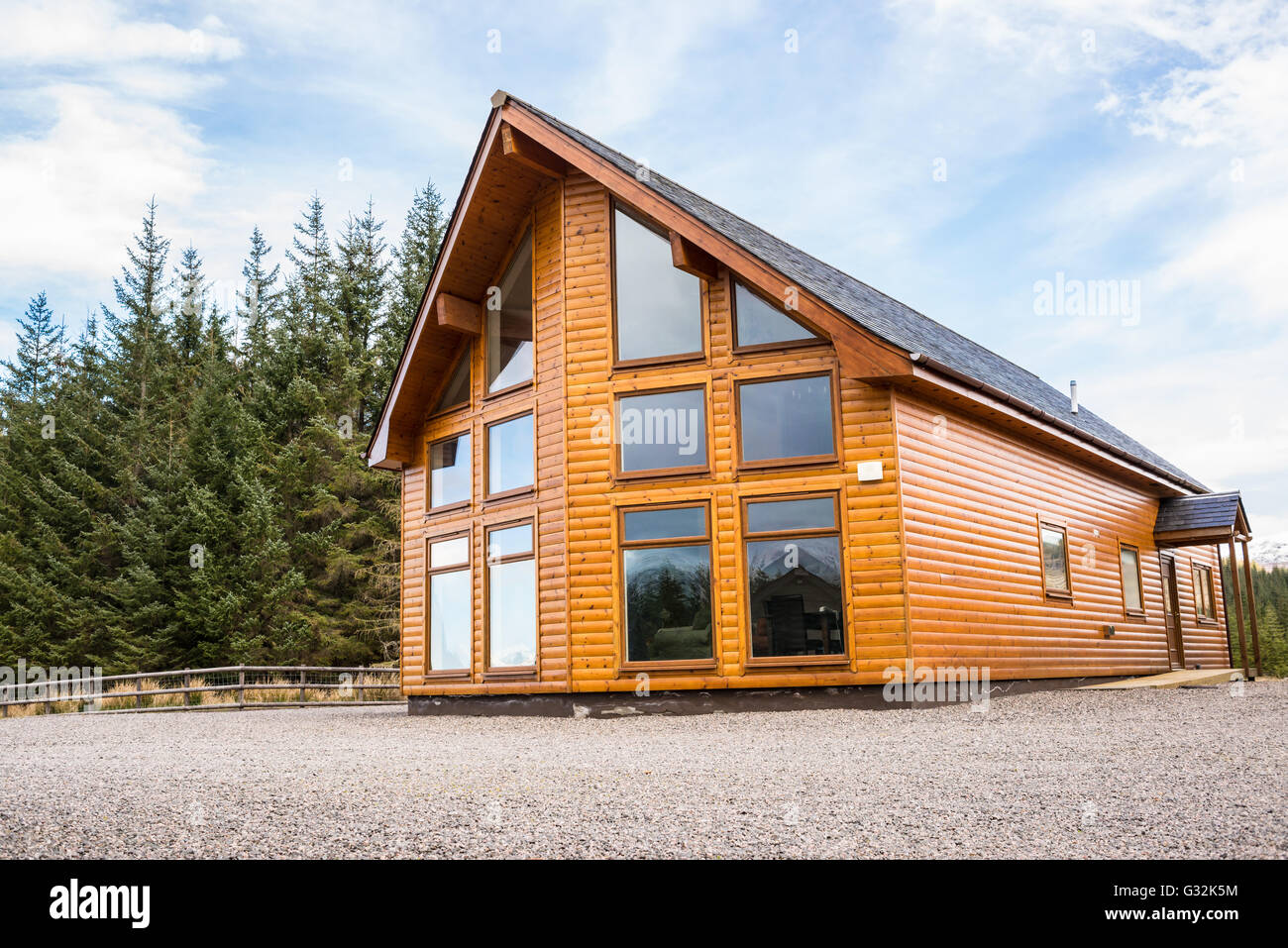 Campagna moderna casa in legno con facciata con grandi finestre di vetro. Gli abeti della foresta nel background. Foto Stock