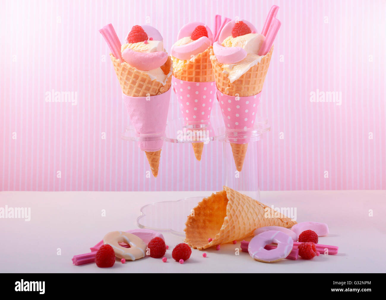 È arrivata l'estate themed vaniglia gelati in coni con rosa candy decorazioni su un bianco tavola di legno contro una striscia rosa Foto Stock