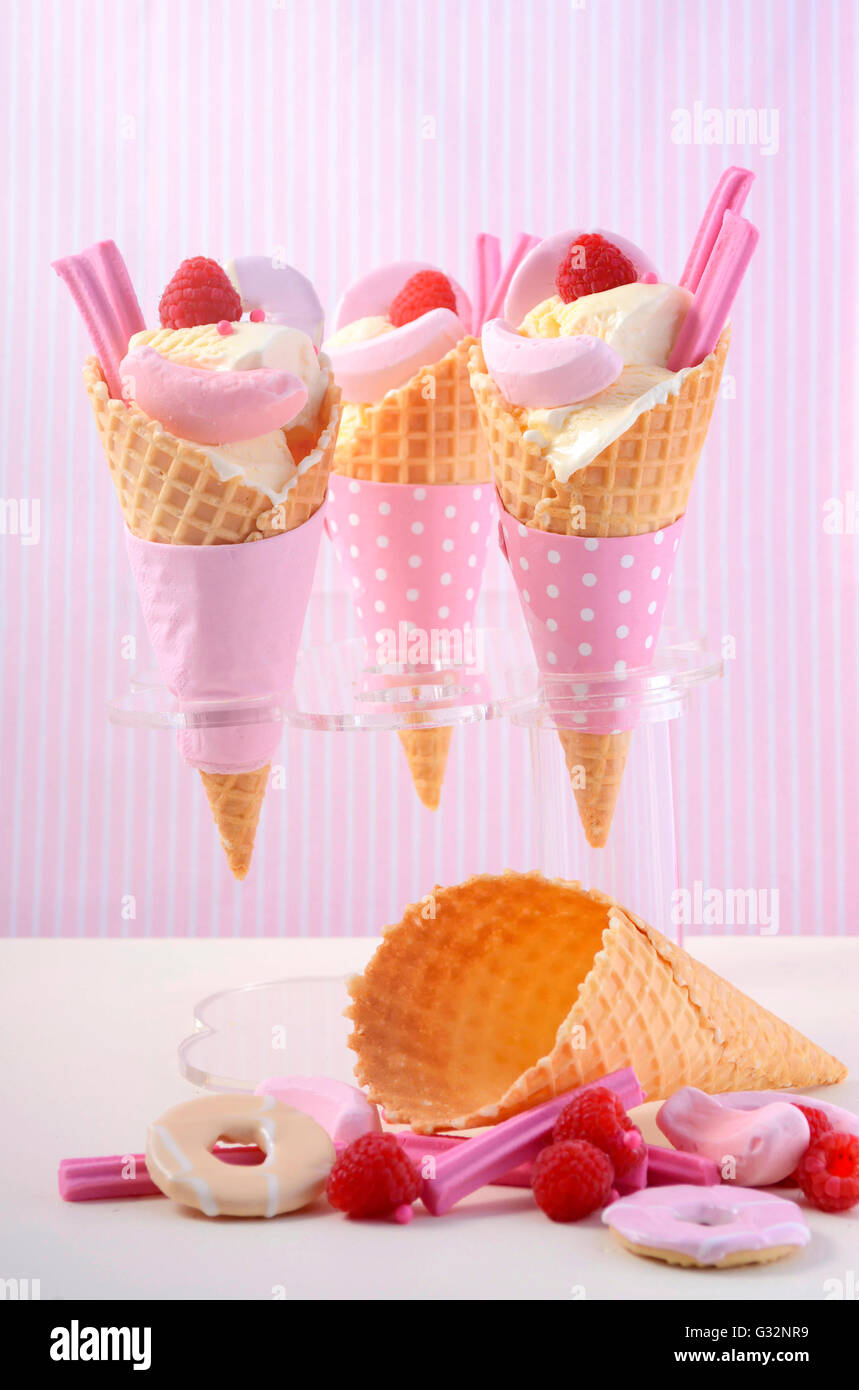 È arrivata l'estate themed vaniglia gelati in coni con rosa candy decorazioni su un bianco tavola di legno contro una striscia rosa Foto Stock