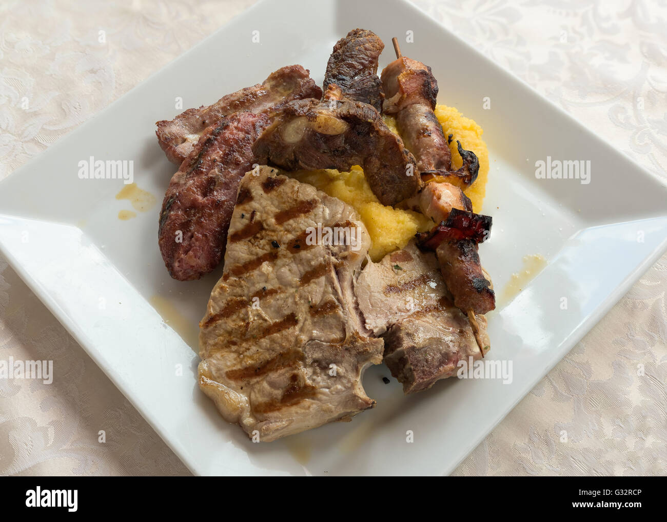 Tipiche italiane grigliate di carne e mescolare la polenta su una piastra al ristorante,dall'alto. Foto Stock